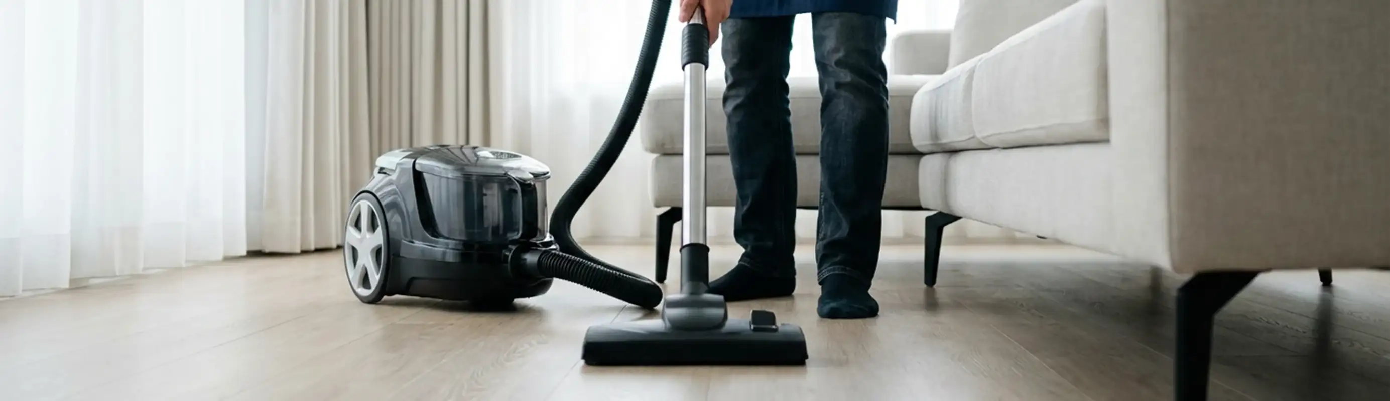 Professional house cleaner vacuuming a living room floor with a canister vacuum cleaner, Bloomington, IN.