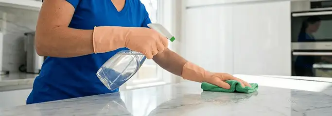 Maid service worker spraying and wiping a kitchen countertop with a microfiber cloth for sanitizing, Bloomington, IN.