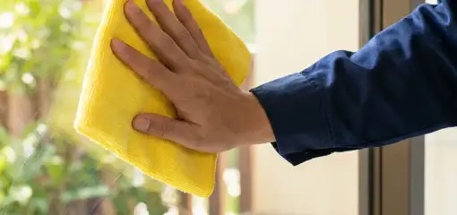 House cleaner wiping a glass window with a yellow microfiber cloth for streak-free cleaning, Bloomington, IN.